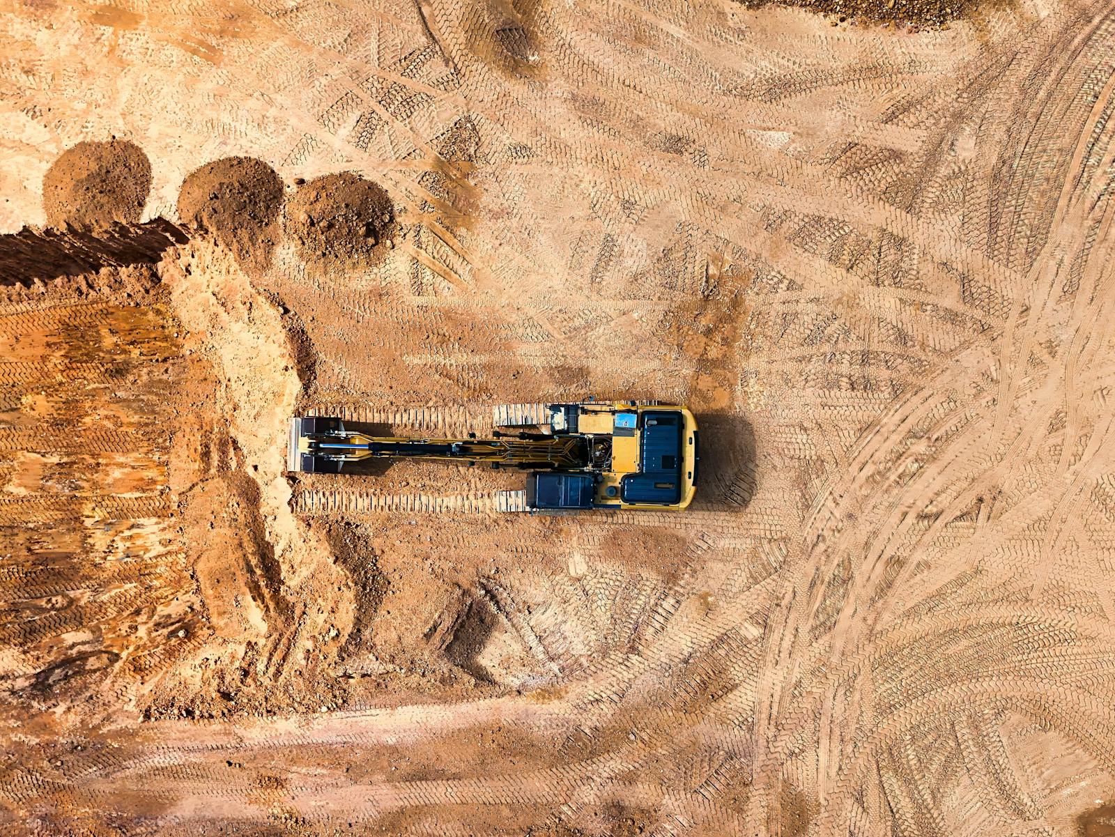 Aerial view of an excavator working on a large empty construction site